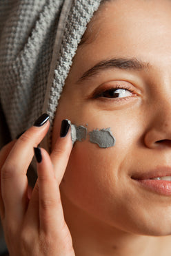 Close-up of woman applying L'ATHENE CLARIFIQUE Purifying Clay Mask to her cheek for detox and pore minimizing.