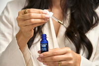Hands holding a blue bottle of L'ATHENE EXTRACT Dry Skin Hydrating Plant Oil, with a dropper dispensing oil.
