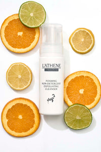 L'ATHENE Citrus Foam Exfoliating Cleanser bottle with sliced oranges, lemons, and limes on white background.