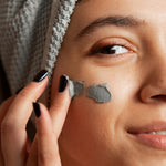 Close-up of woman applying L'ATHENE CLARIFIQUE Purifying Clay Mask to her cheek for detox and pore minimizing.